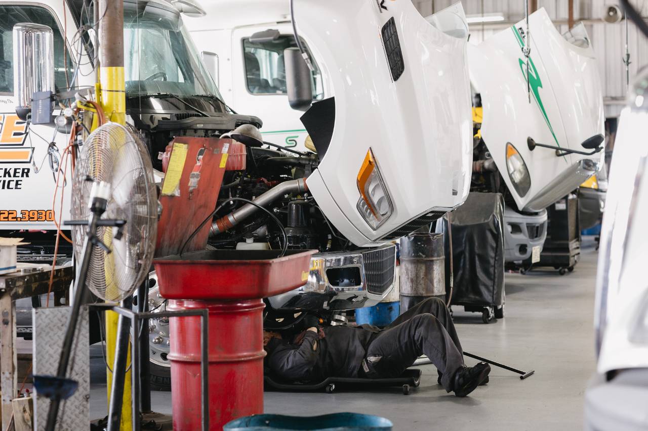 Sun State International technician working under a truck cab during a service bay inspection