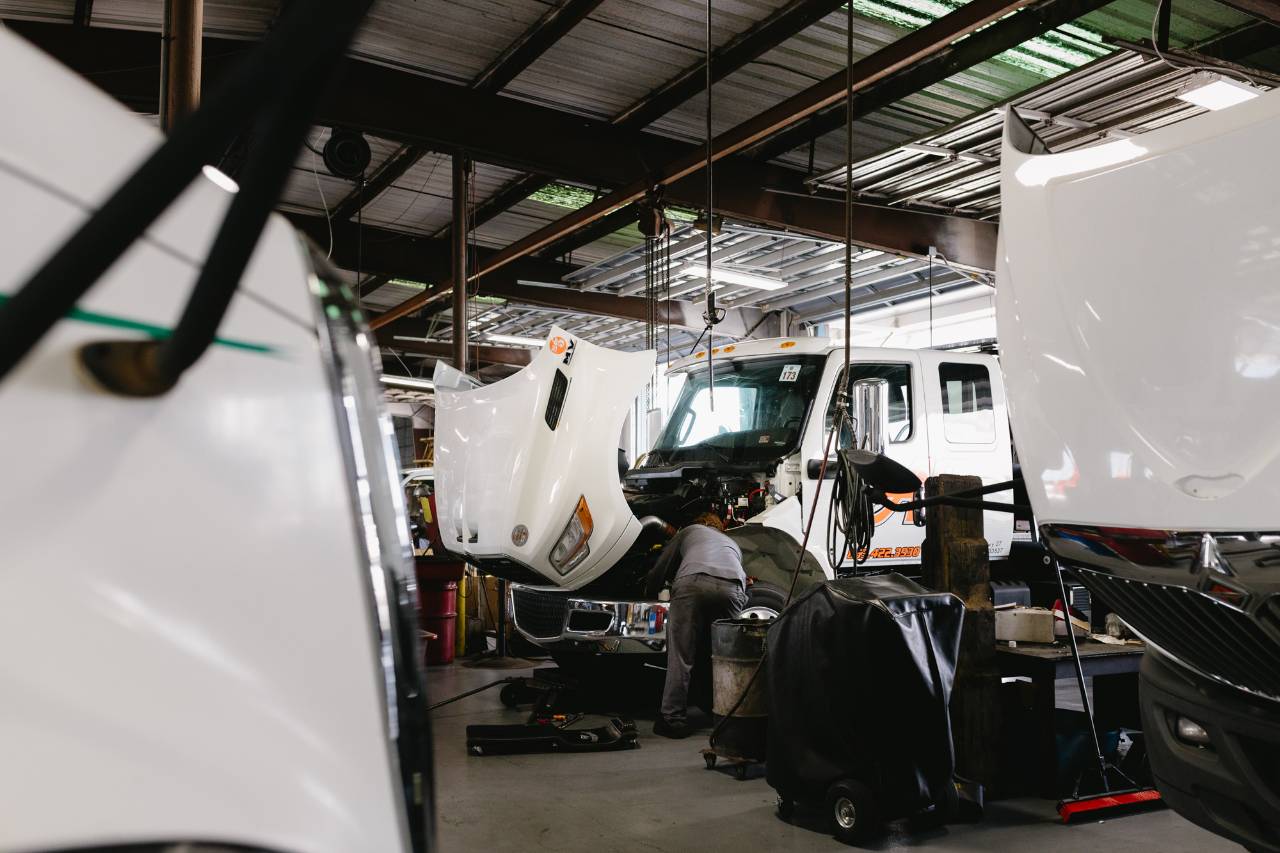 Technician inspecting a truck's front end and engine bay during fleet maintenance service