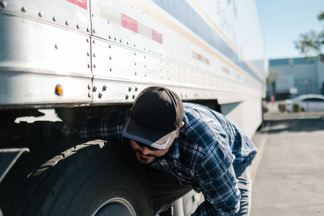 Technician inspecting under a trailer near the wheel wells for wear