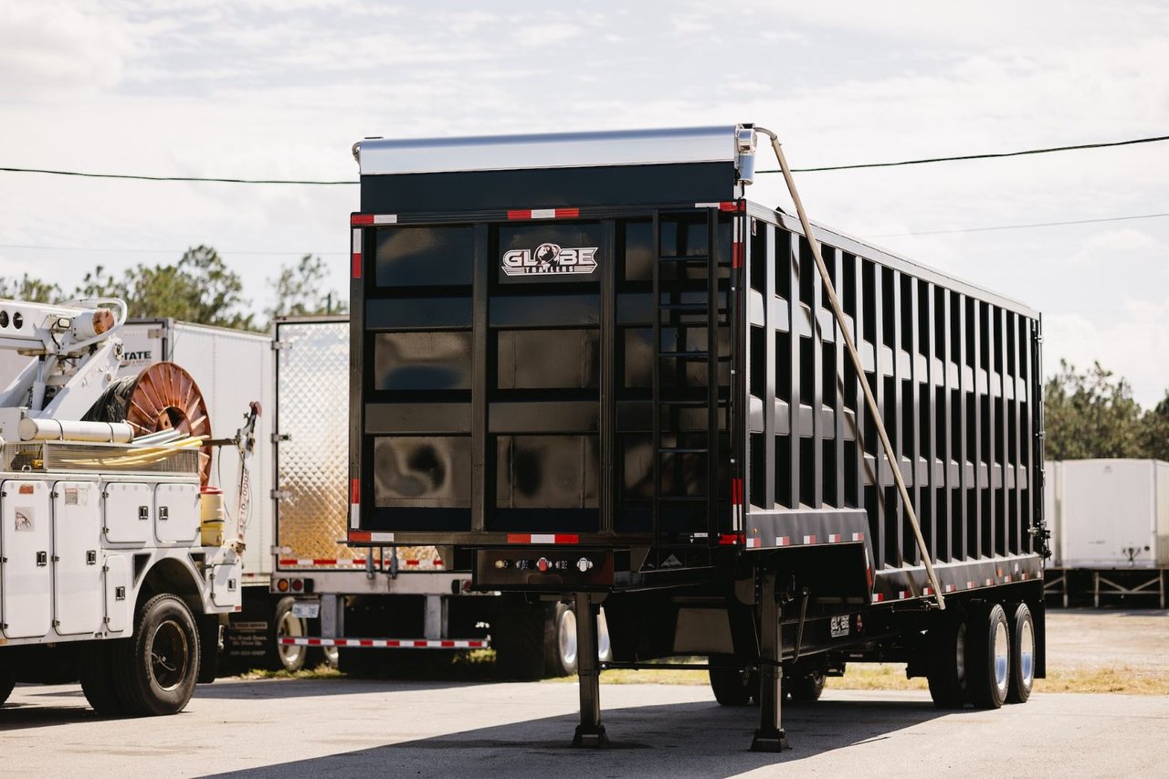 Used Globe dump trailer parked in the Sun State Trailers lot alongside a utility truck