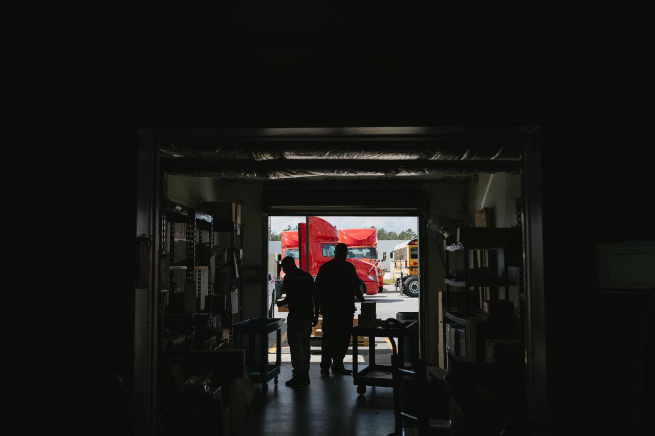 Sun State International team silhouetted near red semi trucks at the shop entrance