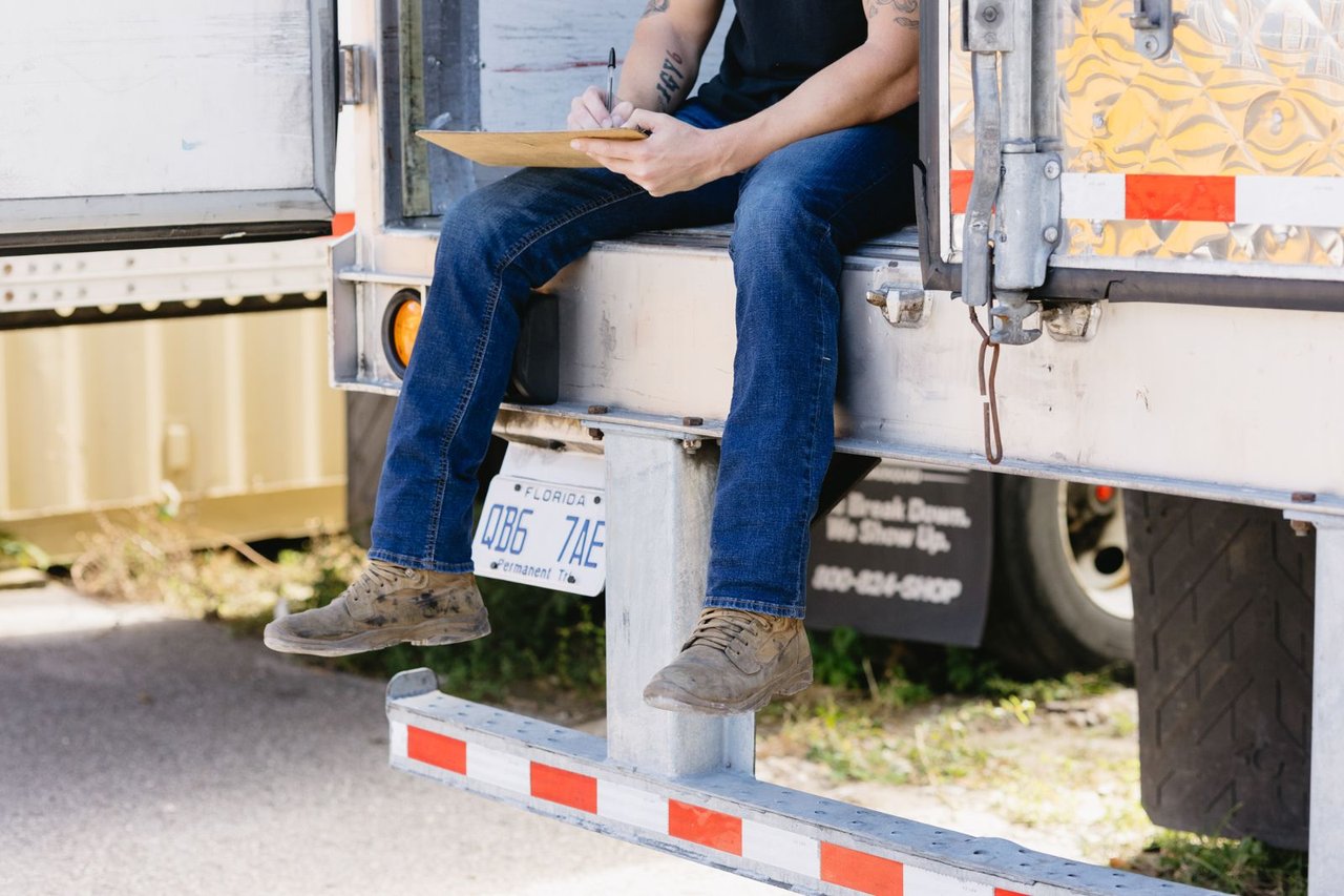 Technician sitting on a trailer tailgate logging inspection notes on a clipboard