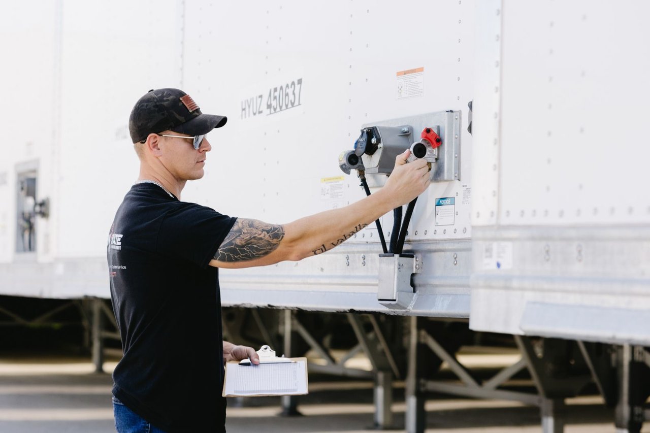 Sun State technician inspecting a trailer's electrical connections with a clipboard in hand